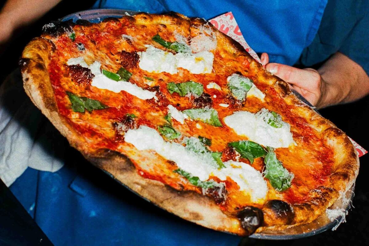 Hands kneading fresh pizza dough on a floured surface.