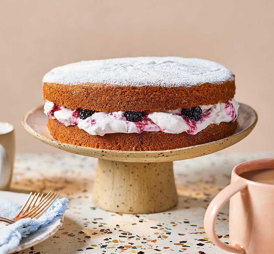 A beautiful air-fryer Victoria sponge cake filled with cream and berries on a cake stand.