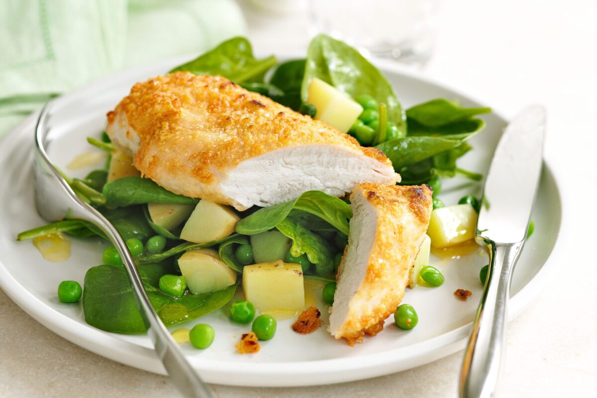 A golden-crusted parmesan chicken breast served on a bed of roasted spring vegetables and potatoes.