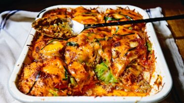 A baking dish of Korean Rice Cake Lasagna with melted, bubbly cheese on top.