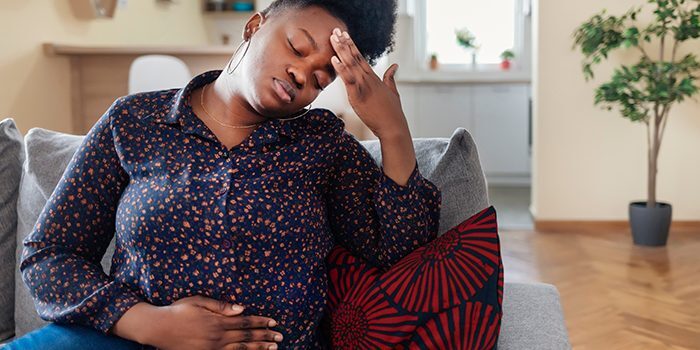 Woman feeling stomach pain while sitting on a sofa.