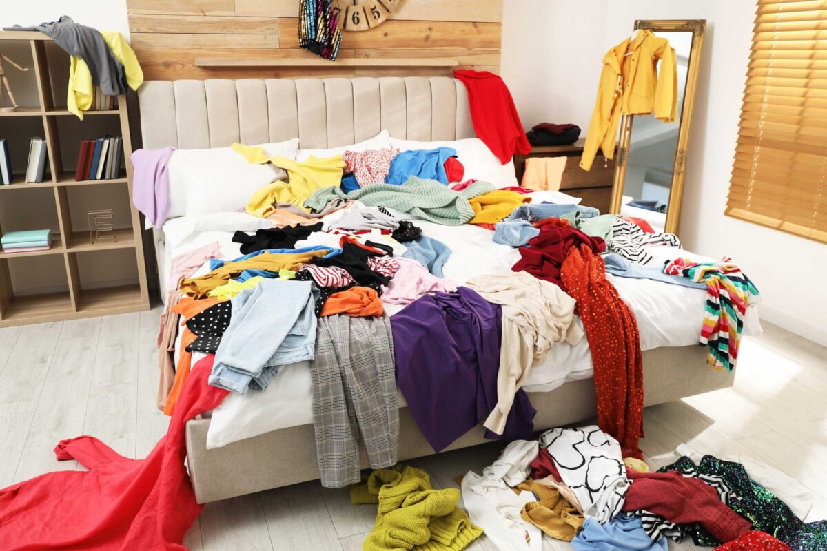 A messy bedroom with clothes scattered on the bed and floor.