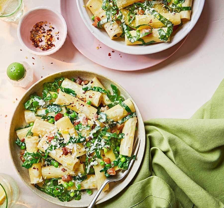 A bowl of creamy rigatoni pasta with spring greens and bacon