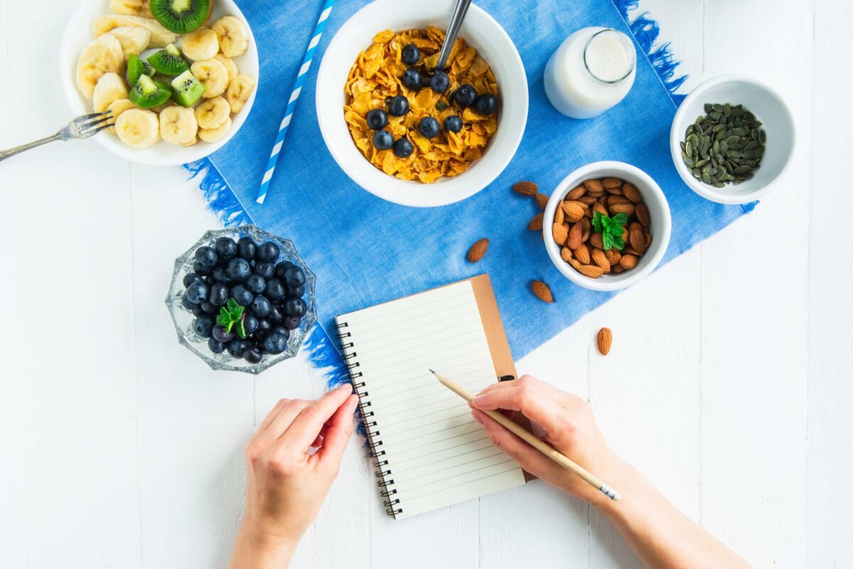 A person writing in a food diary next to a healthy breakfast.
