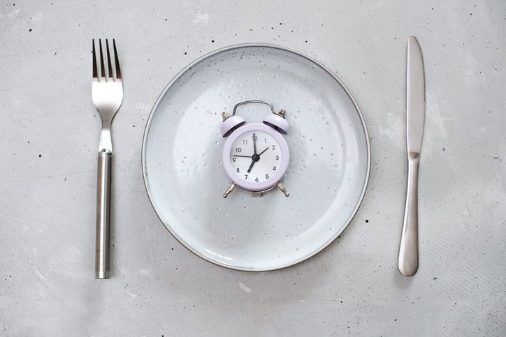 A plate with a fork, knife, and spoon next to an alarm clock, representing breakfast time.