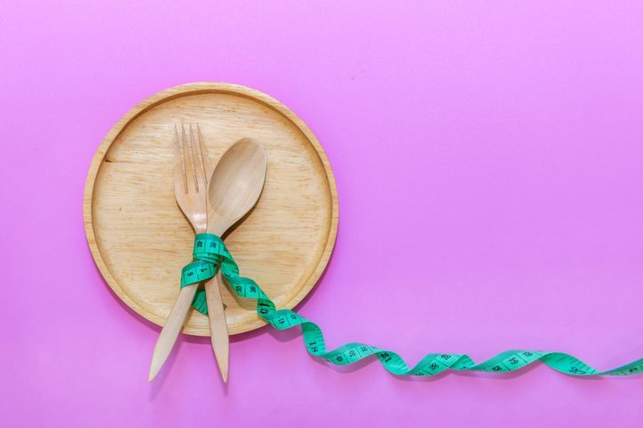 A wooden plate and fork wrapped with a yellow measuring tape, symbolizing a healthy meal.