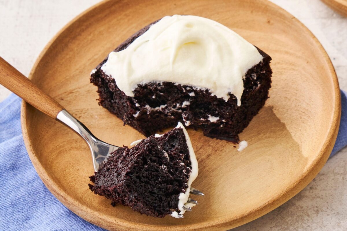 A close-up slice of dark, rich chocolate cake with white frosting.