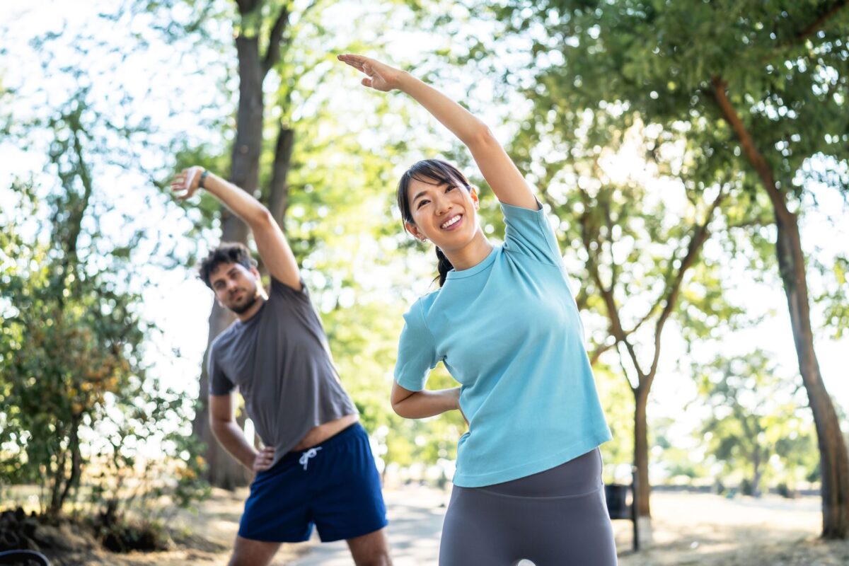 Man and woman stretching to the side in a park.