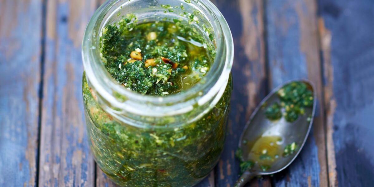 A jar of vibrant green wild garlic pesto next to a bowl of pasta.