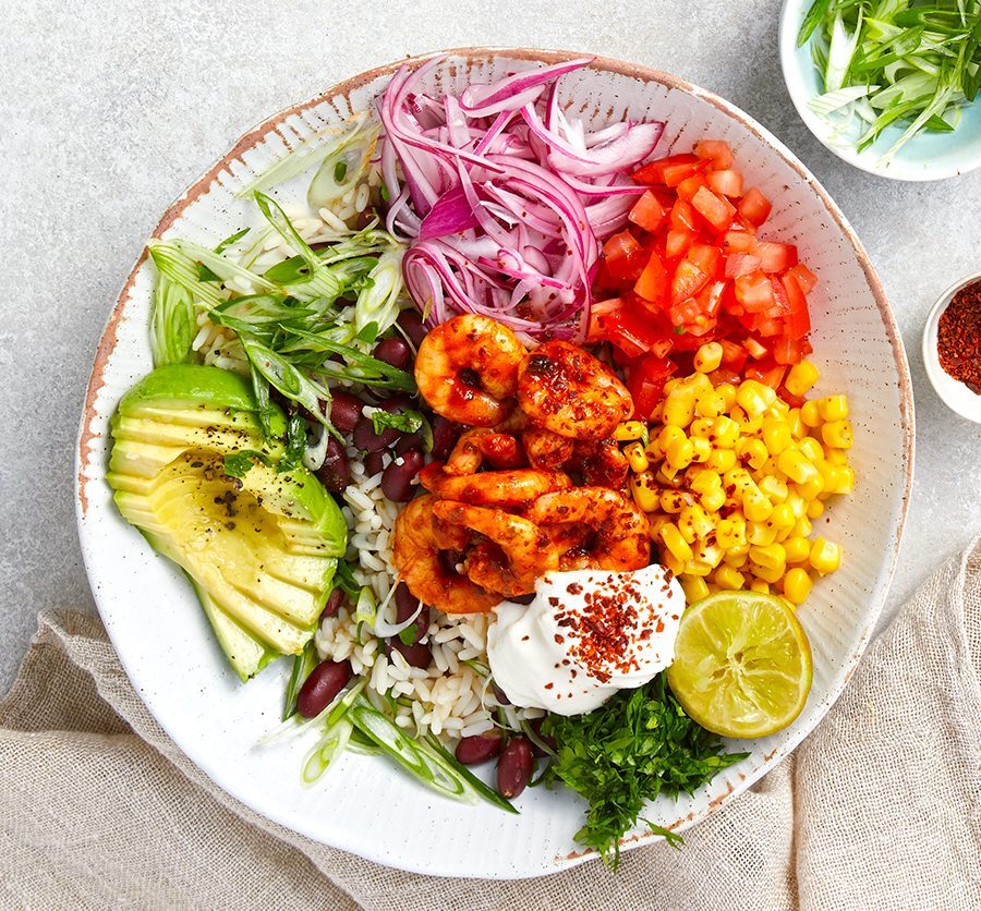 A colorful burrito bowl with rice, beans, corn, and fresh vegetables.