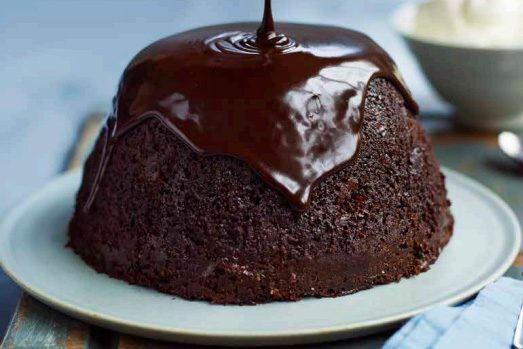A steamed chocolate stout pudding with sauce being poured over it.