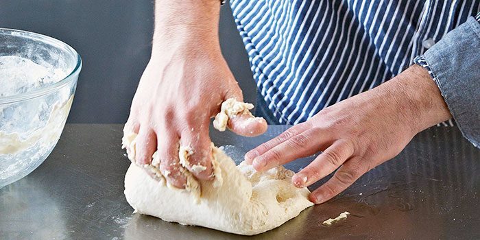 Kneading hot cross bun dough by hand on a floured surface.