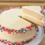 A beautiful slice of classic vanilla cake with white frosting on a plate.