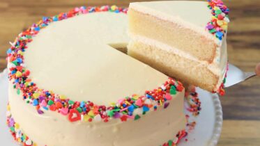 A beautiful slice of classic vanilla cake with white frosting on a plate.