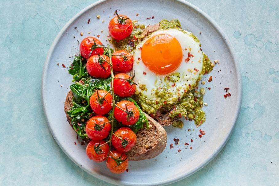 Pesto eggs on a slice of toasted sourdough bread, garnished with fresh herbs.