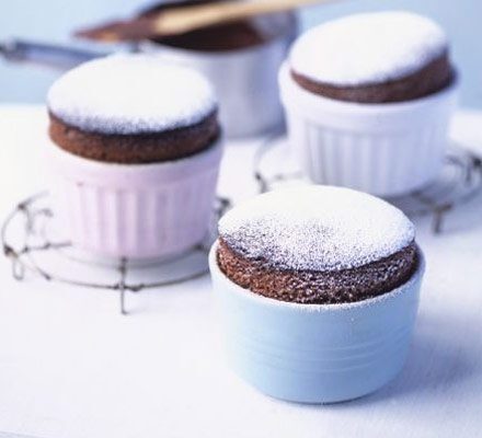 Individual chocolate soufflés in white ramekins, dusted with powdered sugar.