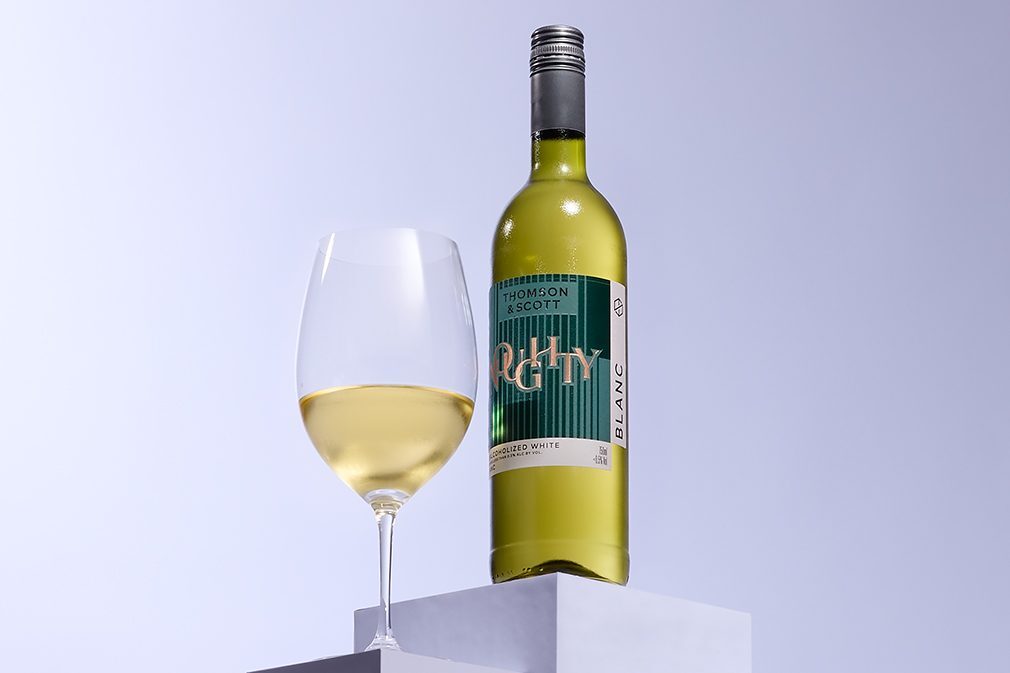 A bottle of white non-alcoholic wine next to a filled glass.