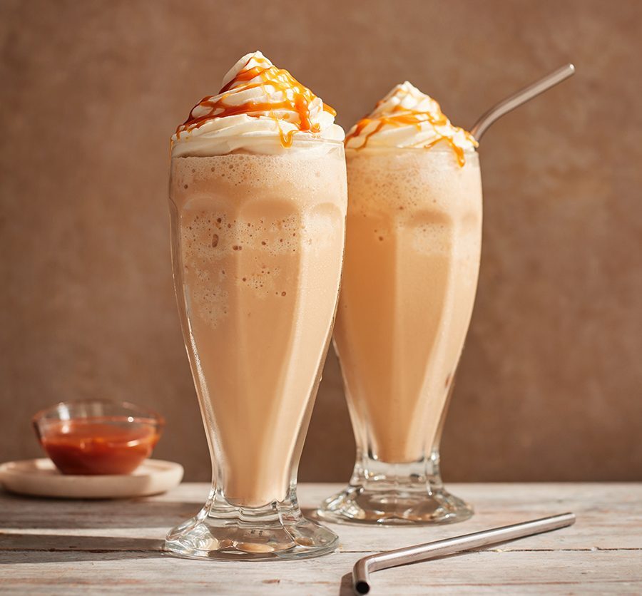 Two caramel frappé drinks topped with whipped cream and caramel drizzle.