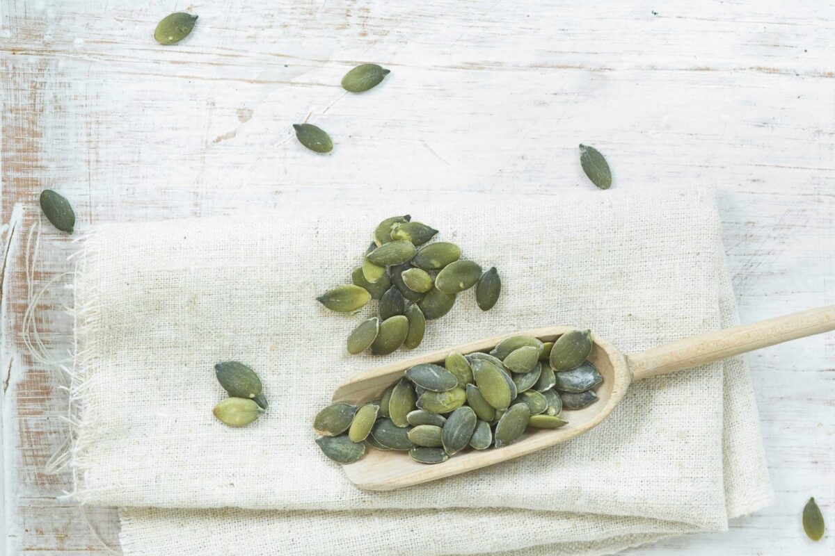 A wooden spoon filled with pumpkin seeds