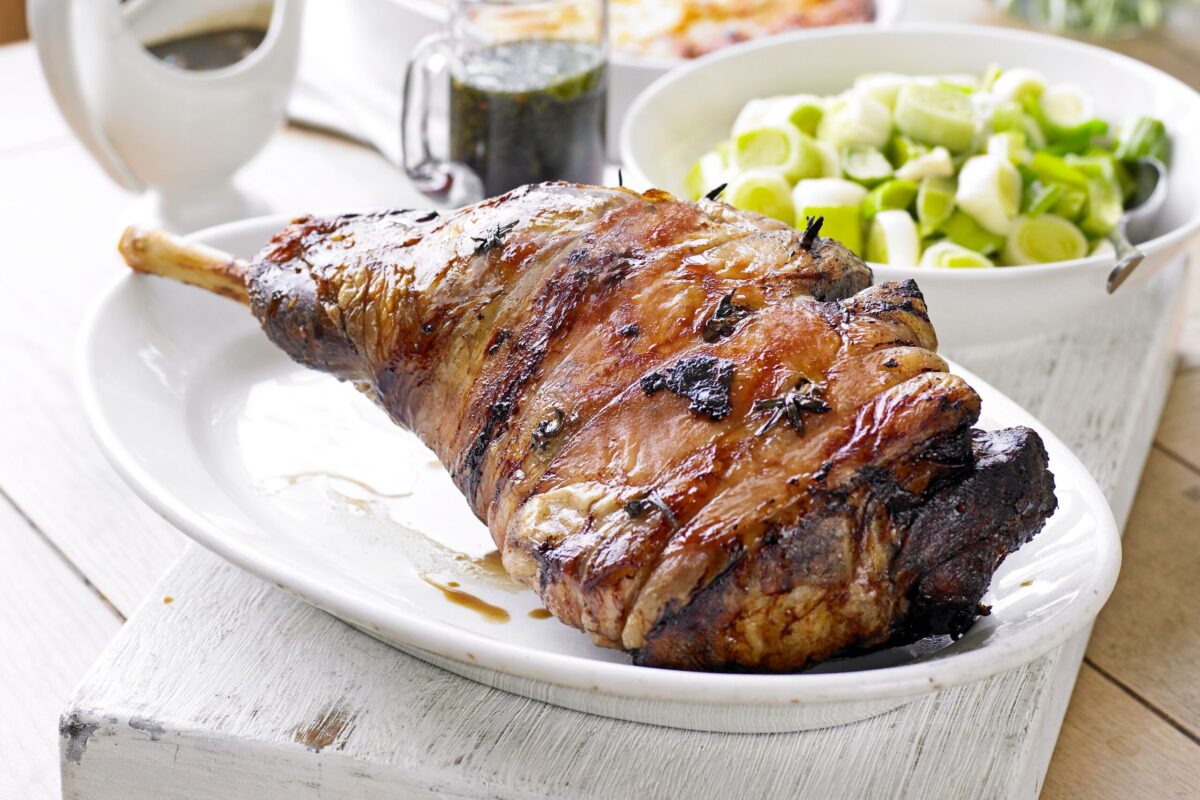 A beautiful roast leg of lamb studded with fresh rosemary and garlic on a serving platter