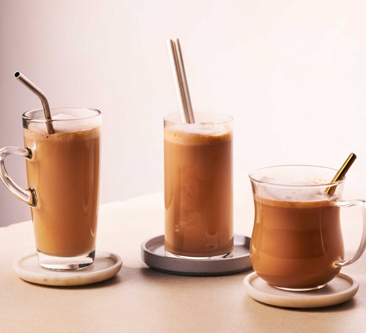 Three glasses of Spanish latte on coasters with straws.